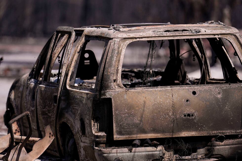 Un vehículo calcinado permanece cerca de una vivienda mientras arde el incendio de la...